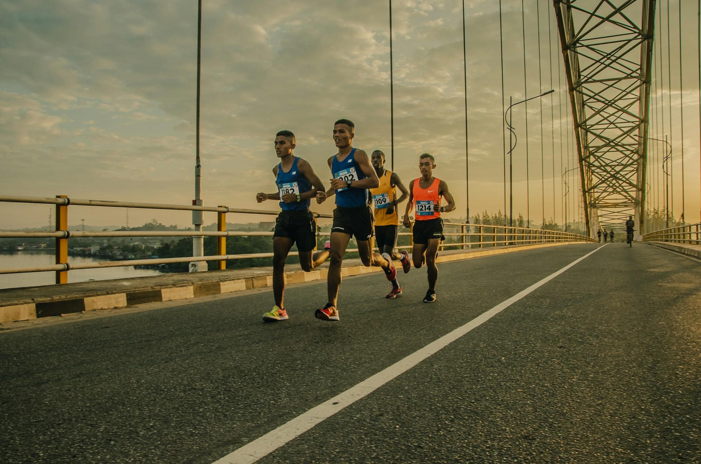 Four runners training together on a bridge road at sunrise